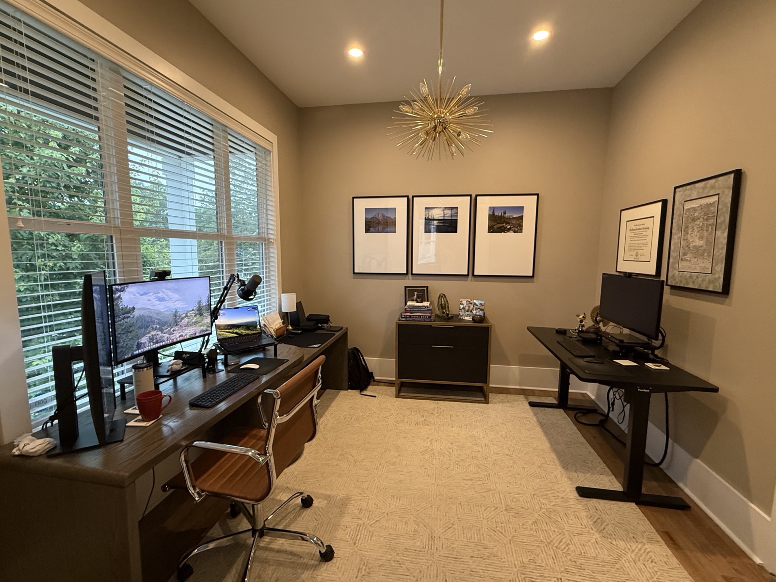 A home office with two desks, a wall of framed photography, and a sunburst chandelier
